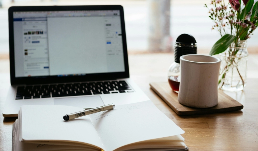 Laptop, open notebook, and coffee on desk.
