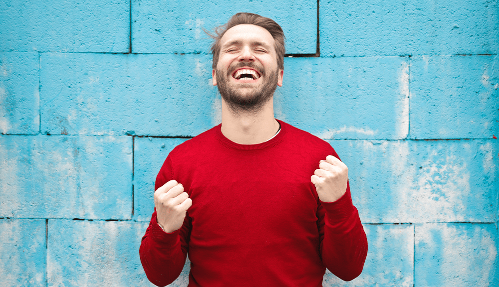 Joyful man smiling against blue wall background.