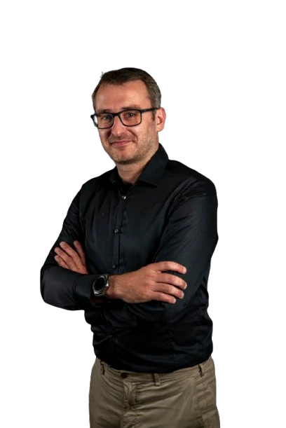 Homme en chemise noire avec des lunettes, bras croisés.