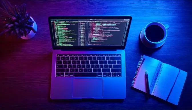 Laptop with code, notebook, and coffee on desk